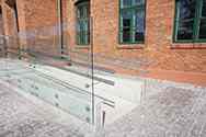 Glasværn i selvbærende hærdet sikkerhedsglas med rørformet dobbelt håndliste i rustfrit stål på kørestolsrampe
