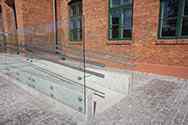 Glasgelænder i selvbærende sikkerhedsglas med dobbelt håndliste i rustfrit stål på kørestolsrampe