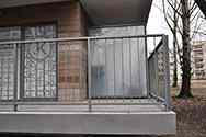 Balcon gelænder med lodrette stål stænger. Inddækninger af stålplade omkring balkonpladen. Skillevægge af rustfrit stål og matteret glas